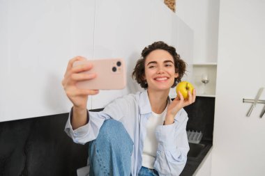Güzel kız blogcu, elma yerken selfie çekiyor, takipçilere nasıl sağlıklı bir yaşam sunulacağını gösteriyor, fotoğraf için akıllı telefonu tutuyor..