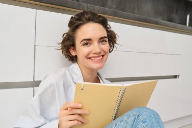 Mutlu genç bir kadının portresi günlüğüne yazar ve gülümser, defterine not alır, kalemini tutar, yere oturur. Boşluğu kopyala