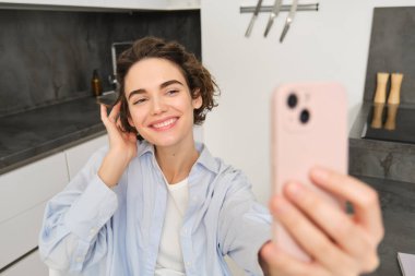 Mutlu, güzel esmer kız evde selfie çekiyor, akıllı telefonuyla poz veriyor..