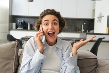 Şaşırmış esmer kadının yakın portresi, heyecandan koltuğa atlıyor, telefonlara cevap veriyor, telefondan harika haberler duyuyor, şaşırmış ve mutlu bir şekilde tepki veriyor..