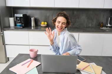 Mutlu genç kadın, öğretmenlik öğrencileri online. Kız uzaktan iş toplantısına ev bilgisayarından bağlanıyor, merhaba diyor, bilgisayara el sallıyor..