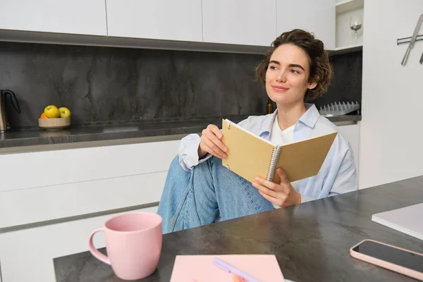 stock image Lifestyle concept. Smiling brunette woman, sitting at home with notebook, reading notes, doing her homework at home.