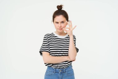 Şüpheli yüzlü genç bir kadın, dudaklarını kapatıyor, ağzını mühürlüyor, kimseye söylemeyeceğine söz veriyor, beyaz arka planda soyutlanmış. Boşluğu kopyala