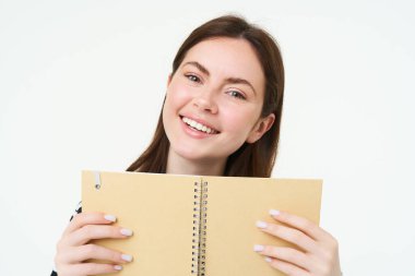 Defterli genç bir kadın resmi, kişisel günlüğünü tutuyor, iş planlayıcısı, gülümsüyor, bir şeyler okuyor, beyaz arka planda duruyor..