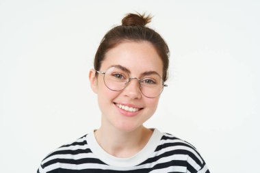 Gözlüklü hoş bir genç kadının yakın portresi, kameraya bakıyor ve gülümsüyor, yeni gözlük deniyor, beyaz arka planda duruyor..