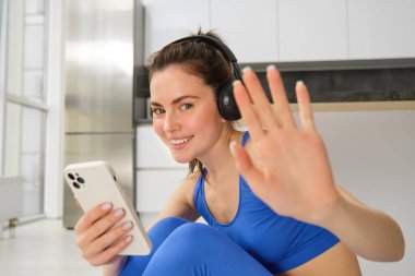 Evde mutlu bir fitness eğitmeni, kulaklıkla ve akıllı telefonla egzersiz yapıyor, müzik dinliyor ve eğitim egzersizleri yapıyor..