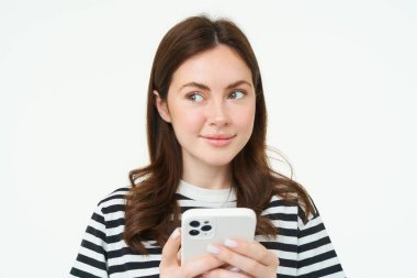 Telefonu olan bir kızın portresi, akıllı telefonu tutan ve düşünen, gülümseyen ve yan bakan, internetten beyaz bir arka plan satın almaya karar veren bir kadın..
