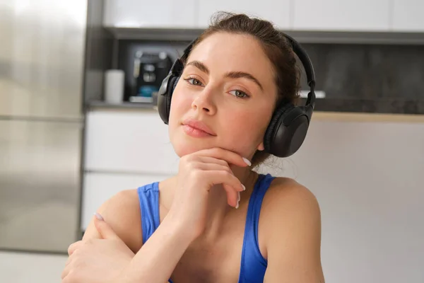 Close up portrait of fitness woman, wearing sportsbra, listening music in headphones, working out at home, doing exercises for fit and healthy body.