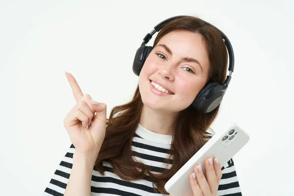 Retrato Estudante Sorrindo Menina Fones Ouvido Segurando Telefone Celular Apontando — Fotografia de Stock