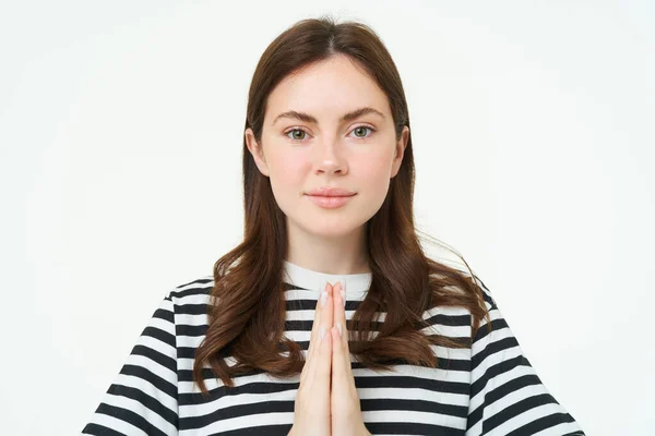 Portrait of young woman expresses her gratitude, shows thank you, namaste gesture, holding hands clasped together near chest and smiling, standing over white background.