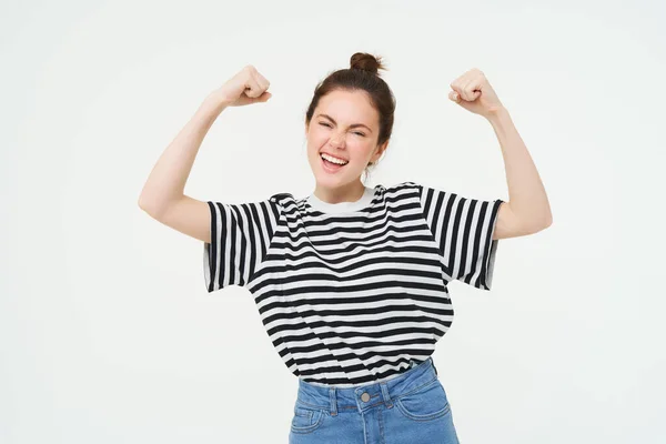 Woman power and feminism. Young girl feeling empowered and strong, flexing her biceps, showing muscles on arms, standing over white background.