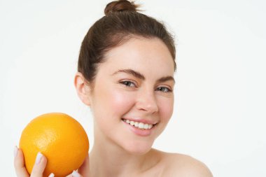 C vitamini ve sağlık konsepti. Genç güzel bir kadın, elinde portakal meyvesi, organik cilt bakımı konsepti, yüz ve vücut ürünleri, beyaz arka planda duruyor..