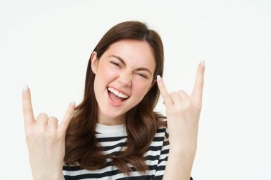 Salla gitsin. Heyecanlı, gülen genç bir kadın, ağır metaller, boynuzlar, jestler ve gülümsemeler, eğlenmek, pozitiflik ve neşe ifade etmek, beyaz arka planda durmak..