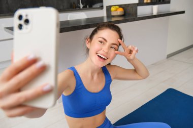 Güzel esmer sporcunun portresi, akıllı telefonda selfie çekmek, cep telefonuyla fitness minderinde poz vermek, spor egzersizlerini kaydetmek, antrenman yapmak..