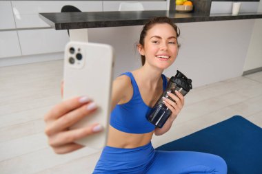 Spor yapan bir kadının portresi, akıllı telefondan selfie çekiyor, fitness hocası egzersizlerini kaydediyor, susuz kalmıyor, antrenman sırasında su içiyor..