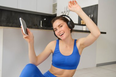 Mutlu fitness kadını dans ediyor, evde egzersiz yaparken eğleniyor, kulaklık takıyor, akıllı telefon tutuyor, egzersizler sırasında müzik dinliyor..