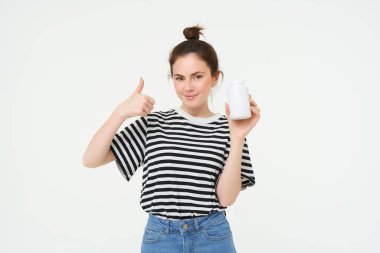 Gülümseyen kız imajı beslenme takviyesi öneriyor, C vitamini şişesi, balık yağı tedavisi, beyaz arka planda duruyor..