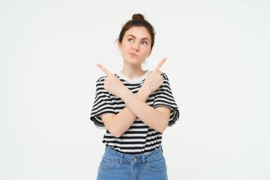 Kafası karışmış bir kadının portresi, farklı seçenekler arasından seçim yapıyor, beyaz arka planda düşünceli bir şekilde duruyor..