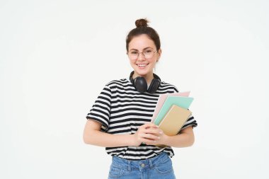 Genç bir kadın resmi, kitapları ve defterleri olan, boynuna kulaklık takan, beyaz arka planda soyutlanmış bir öğretmen. Öğrenci yaşam tarzı konsepti.