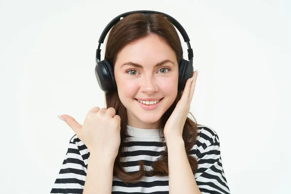 ミュージックストアコンセプト 笑顔の若い女性はヘッドフォンで歌を聞き コピースペースを指し 広告テキストを表示し 白い背景の上に立っています — ストック写真