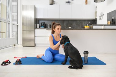 Genç bir kadının evden idman yapması oturma odasında yoga minderine oturup siyah köpeğiyle oynaması kızın dikkatini egzersizlerden uzaklaştırıyor..