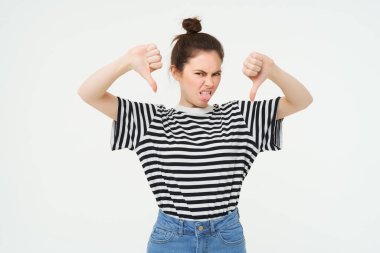 Genç bir kadın olumsuz geri bildirim yapar, baş parmağını kaldırır, ürünü onaylamaz, kötü şeyleri sevmez, beyaz arka planda durur..