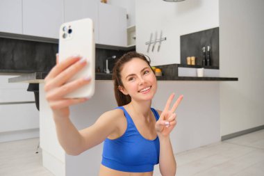 Güzel esmer sporcunun portresi, akıllı telefonda selfie çekmek, cep telefonuyla fitness minderinde poz vermek, spor egzersizlerini kaydetmek, antrenman yapmak..