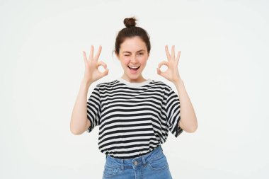 Mükemmel seçim. Gülümseyen stil sahibi genç bayan, tamam, tamam jest, sıfır işaret, beyaz arka plan üzerinde duran.