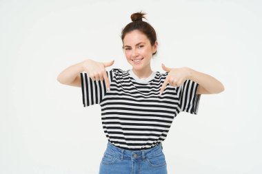 Gülümseyen, güzel genç bir kadının portresi, parmakları aşağıda, reklamları gösteriyor, beyaz arka planda poz veriyor..