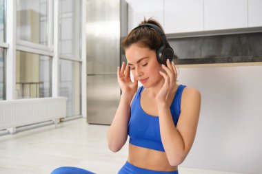 Genç kadın evde çalışırken müzik dinlemek için kablosuz kulaklık takar, spor sutyeni giyer, güler yüzle güler..