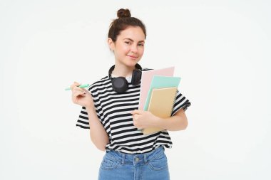 Boynunda not defterleri ve kulaklıkları olan, üniversite reklamı için poz veren beyaz arka planı olan genç bir kadının portresi..