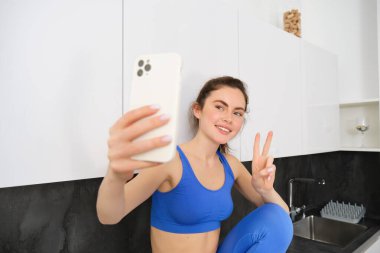 Güzel bir kadının portresi, fitness blogcusu, spor sutyeni ve tozluklarla selfie çeken, akıllı telefonuyla mutfakta poz veren..