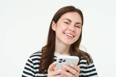 Akıllı telefonlu bir kızın portresi gülüyor, cep telefonu uygulaması kullanıyor, beyaz arka planda izole edilmiş..