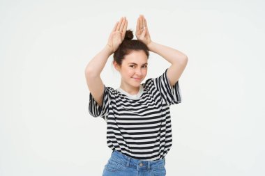 Beyaz kadın portresi, hayvan kulakları yapıyor, sevimli pozlar veriyor, kameraya gülümsüyor, beyaz arka planda duruyor..