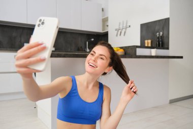 Genç sporcu kadının yakın portresi, fitness kızı egzersiz yaparken selfie çekiyor, yoga minderinde poz veriyor, akıllı telefonu tutuyor ve gülümsüyor..