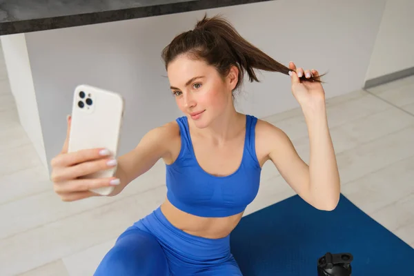 漂亮女运动员的画像 在家里用橡胶瑜伽垫做运动的女人 用智能手机自拍 为健身教练的社交媒体拍照 — 图库照片