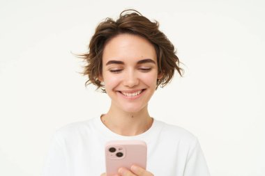 Gülümseyen, akıllı telefon kullanan, mesajlaşan, mobil uygulamalarını kontrol eden genç bir kadının portresi beyaz arka planda duruyor. Boşluğu kopyala