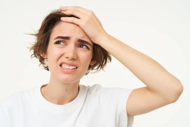 Genç üzgün bir kadının portresi, alnına vurur, yüzüne vurur, kafasına dokunur ve acı çekiyor gibi görünür, baş ağrısı ya da migreni vardır, beyaz arka plan üzerinde izole edilmiş..