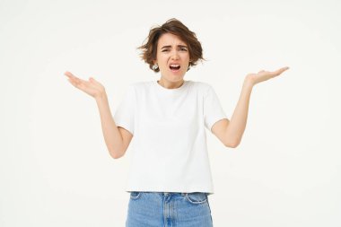 Kafası karışmış bir kadının portresi, omuz silkiyor ve üzgün görünüyor, bir şeyi anlayamıyor, hayal kırıklığına uğramış, beyaz stüdyo arka planında duruyor..