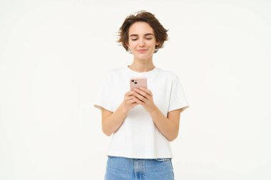 Akıllı telefon kullanan esmer kadının portresi, cep telefonuyla durmak, mesaj atmak, sipariş vermek, sosyal medyayı aramak, beyaz arka planda durmak..