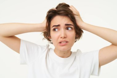 Paniklemiş, etrafa bakınan, el ele tutuşan, belayla yüzleşen, karmaşık bir sorunla karşı karşıya olan, beyaz arka planda duran bir kız..