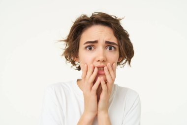 Korkmuş esmer kadın, korkudan titriyor, endişeli ve korkmuş görünüyor, beyaz stüdyo arka planında duruyor..