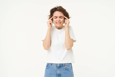 Sıkıntılı, üzgün genç bir kadın kafasına dokunuyor, başı ağrıyor, migreni var, beyaz arka planda duruyor. Boşluğu kopyala