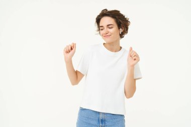 Dans eden, eğlenen, müzikten zevk alan beyaz stüdyo arka planında poz veren mutlu genç kadın portresi. Boşluğu kopyala