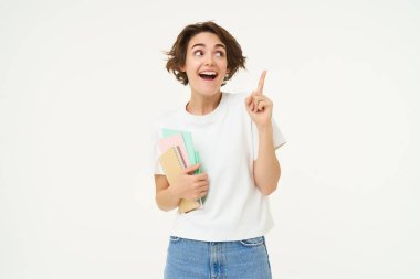 Kahkahalar atan esmer bir kadının portresi, sağ üst köşeyi gösteren defterleri olan bir öğrenci, afiş ya da reklam gösteren, beyaz stüdyo arka planının başında duran.