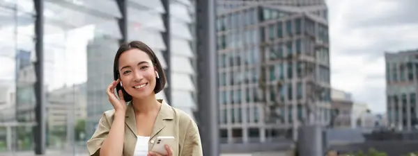 Jonge Lachende Aziatische Vrouw Draadloze Oortelefoons Loopt Straat Met Smartphone — Stockfoto