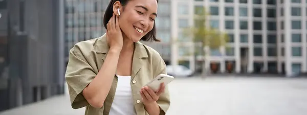 Усміхнена Азіатська Дівчина Слухає Музику Бездротових Навушниках Дивиться Телефон Вибирає — стокове фото