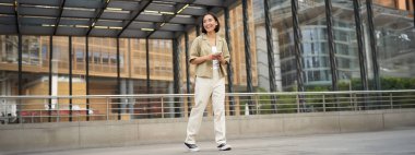 Asyalı kadın modelin telefonlu portresi. Genç Koreli kız akıllı telefonu sokakta tutuyor, telefon kullanıyor..