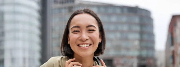 首周りのヘッドフォンでポーズをとる美しいアジアの女性の垂直ショット 笑顔と笑い 昼間の通りに立って — ストック写真