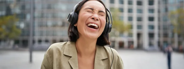 헤드폰을 여성의 도시를 때웃고 웃으며 음악을 즐긴다 — 스톡 사진